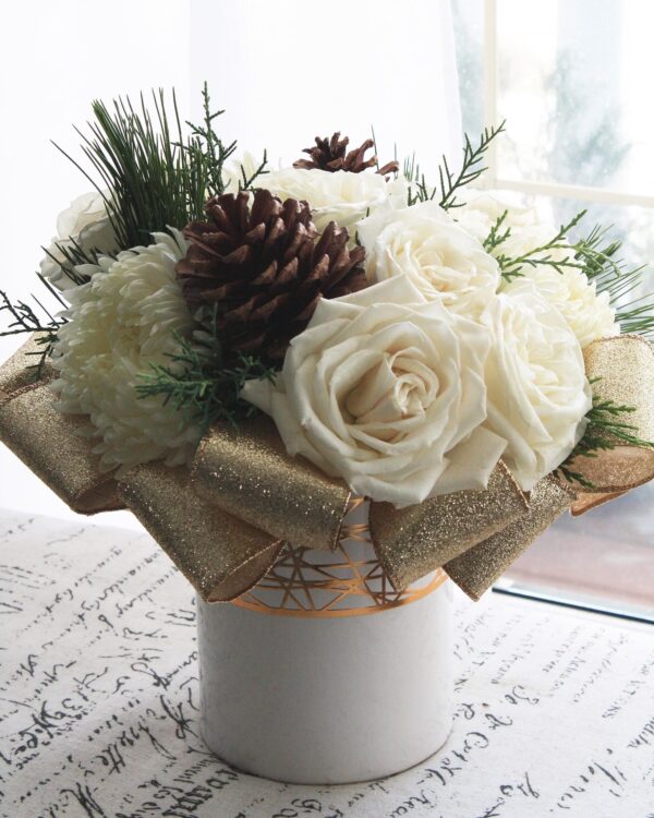 white roses and gold ribbon, with winter green and pinecones in a white vase